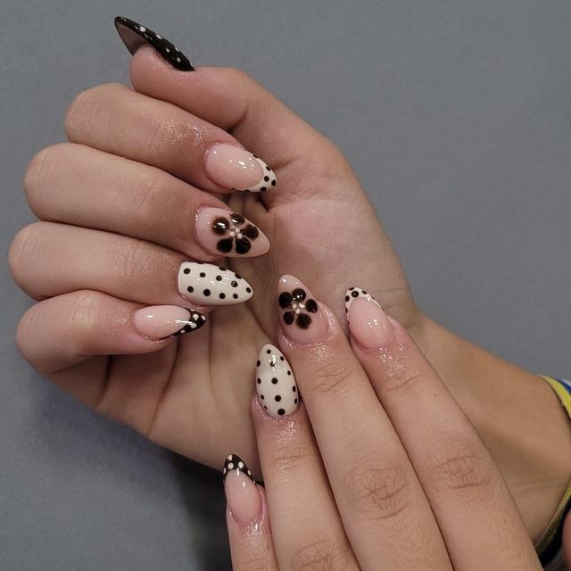 Uñas almendradas nude con lunares y flores negras sobre fondo blanco