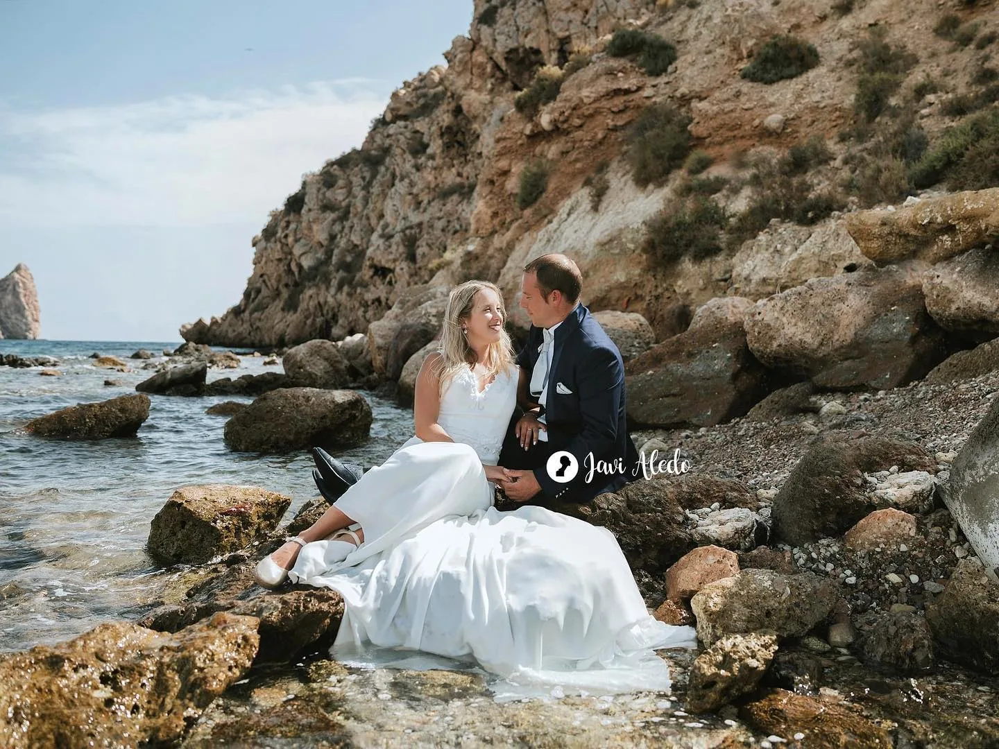 Novios sentados entre las rocas de una cala