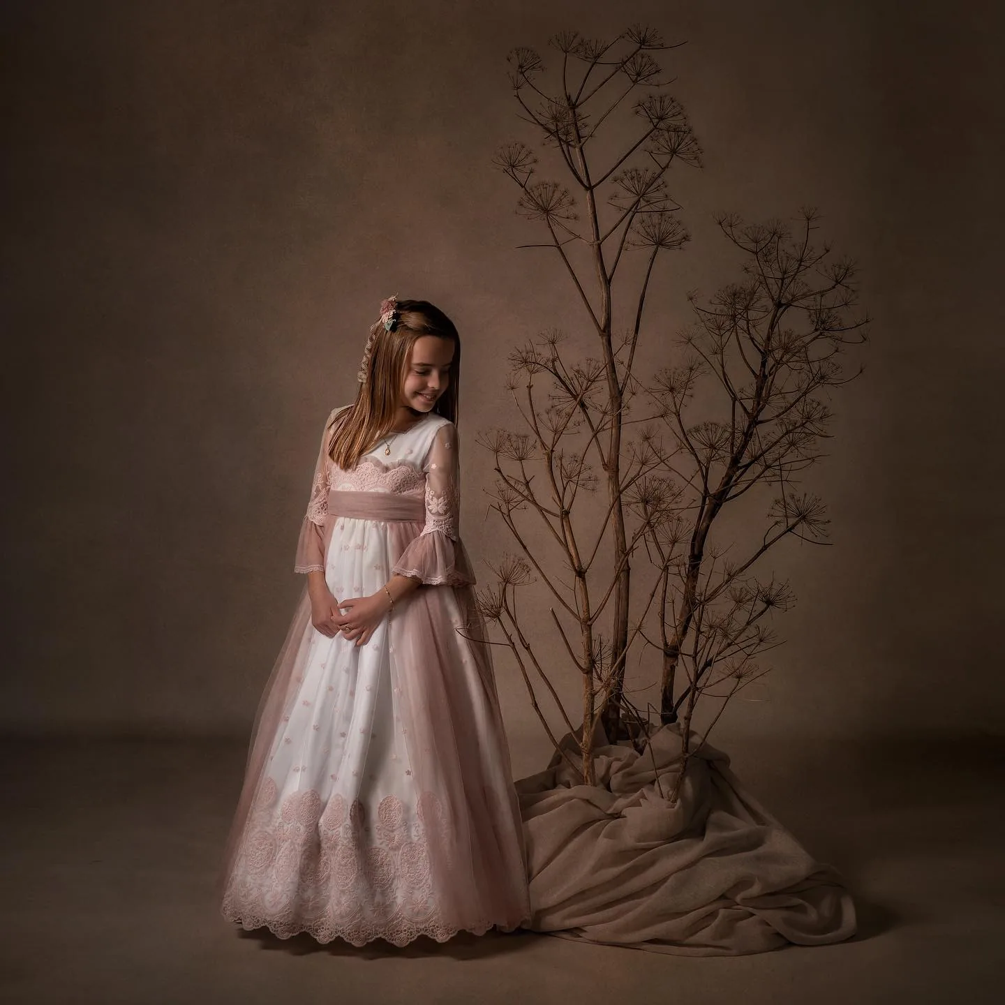 Niña de comunión con vestido rosa junto a unas ramas secas