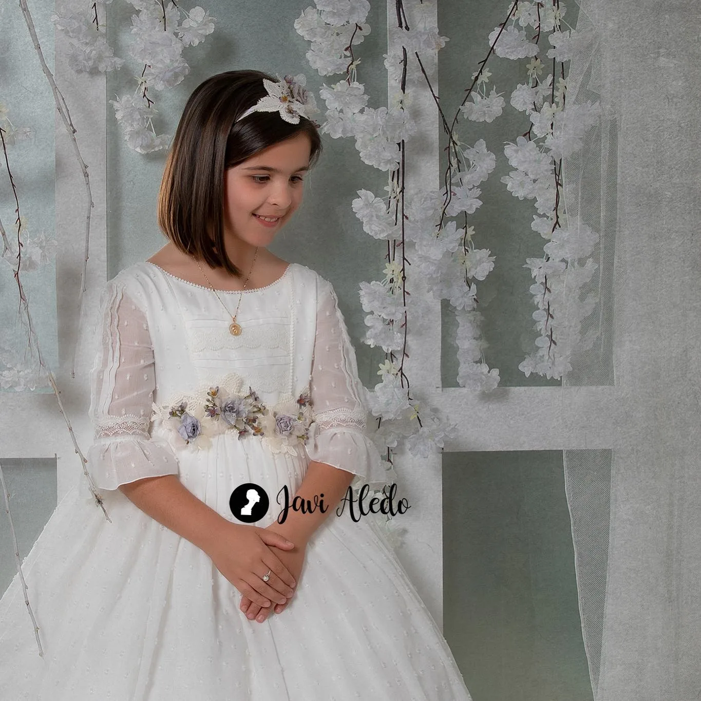 Niña de comunión con ramo ante un fondo de flores blancas