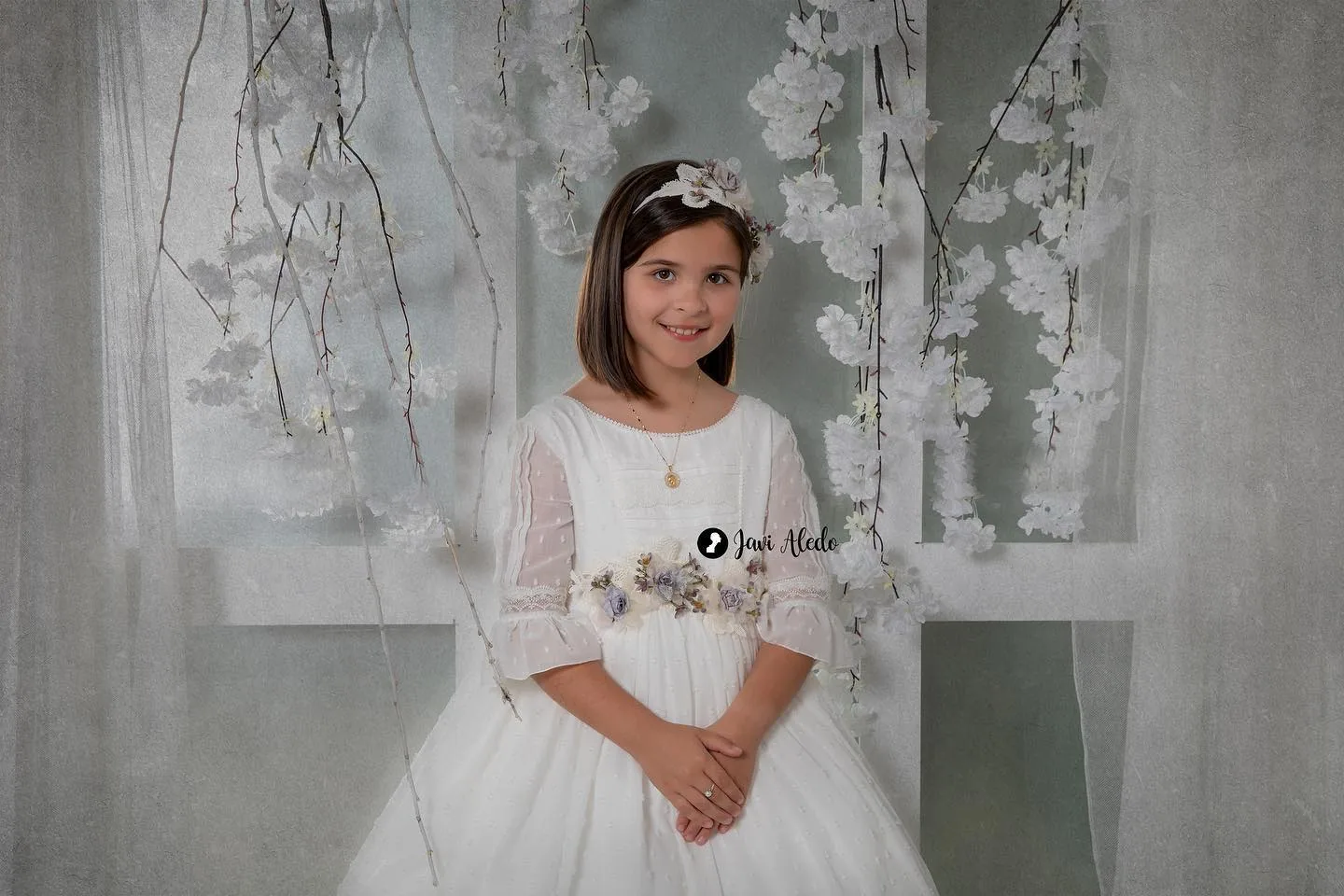 Niña de comunión sentada ante cortinas de flores