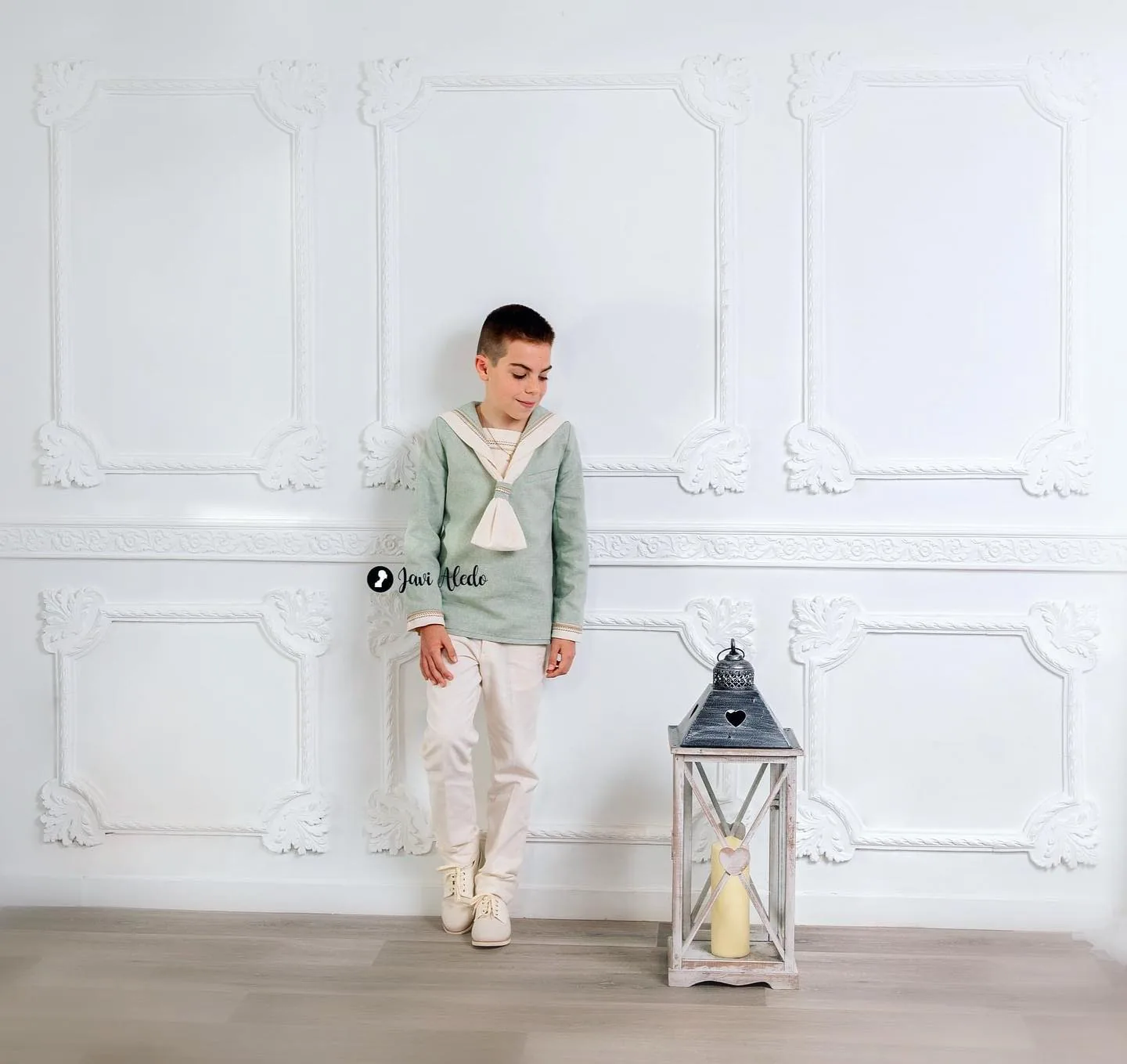 Niño de comunión junto a un farol en un decorado blanco