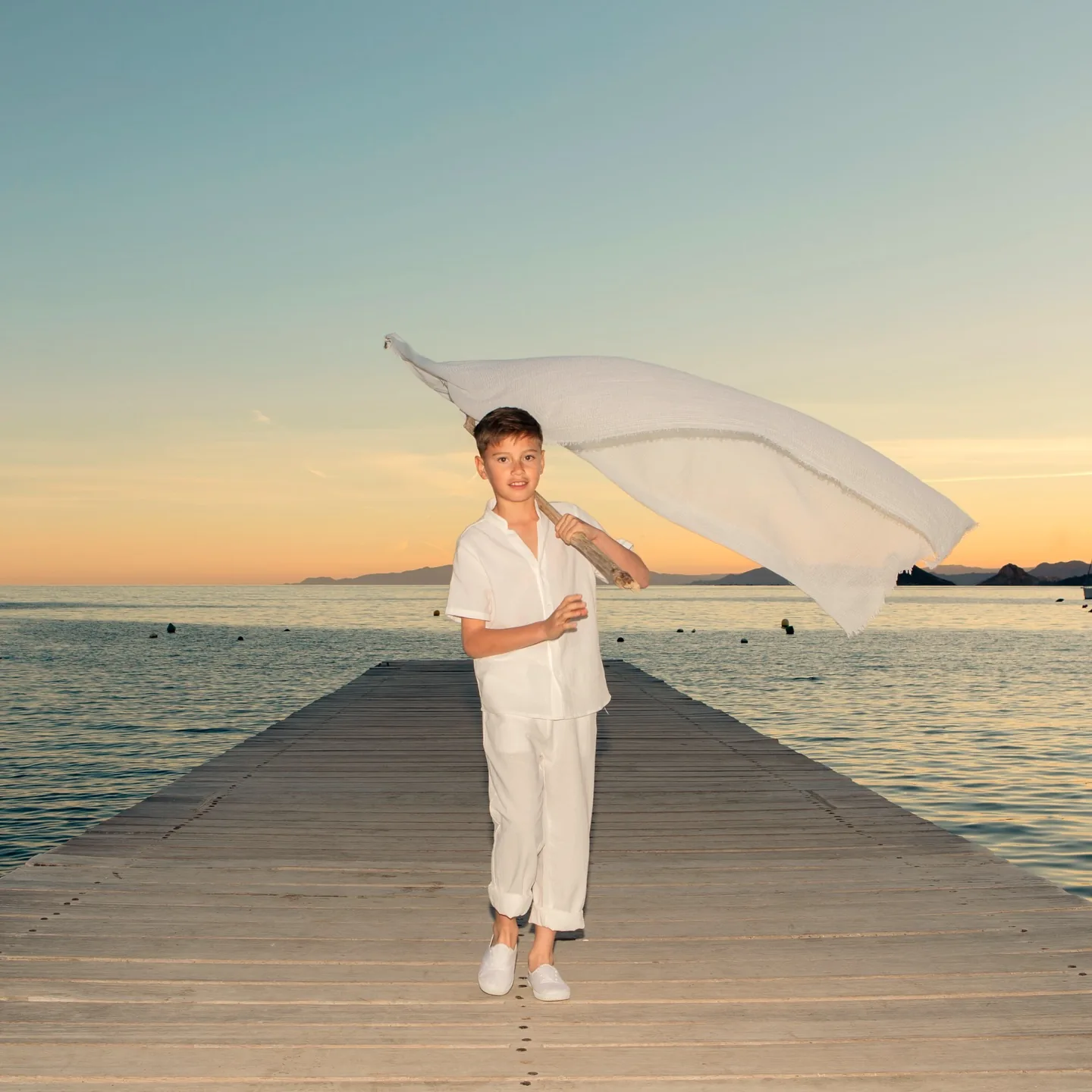 Niño de comunión en un embarcadero sobre el mar al atardecer