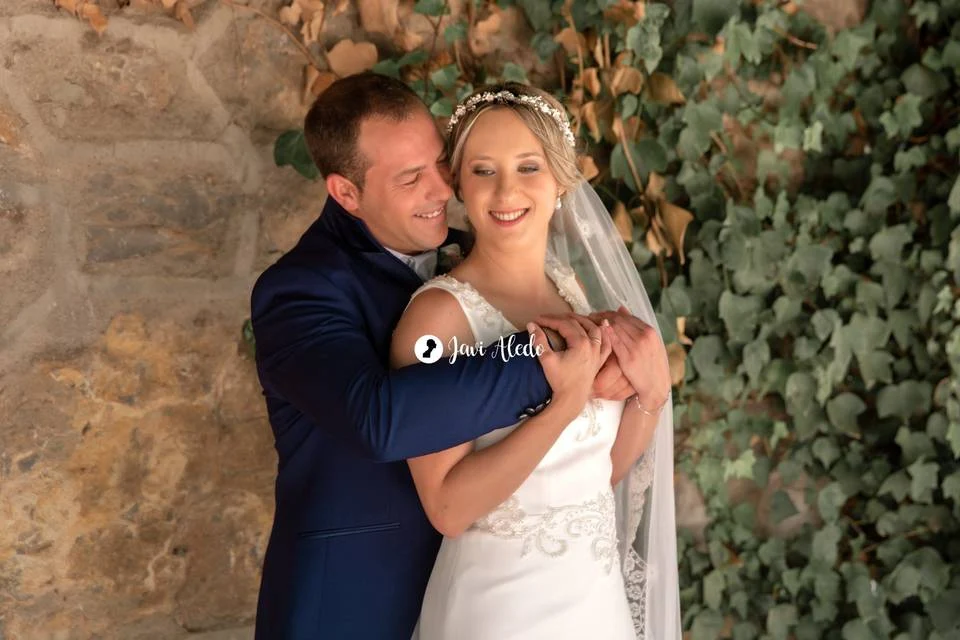 Novios abrazados junto a un muro de piedra