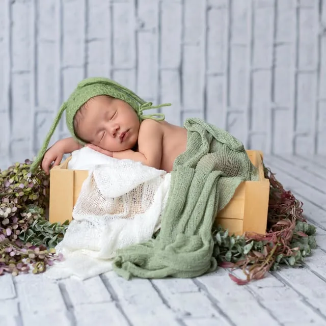 Recién nacido con gorro verde dormido en una caja de madera