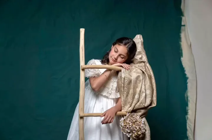 Niña de comunión apoyada en una escalera de madera